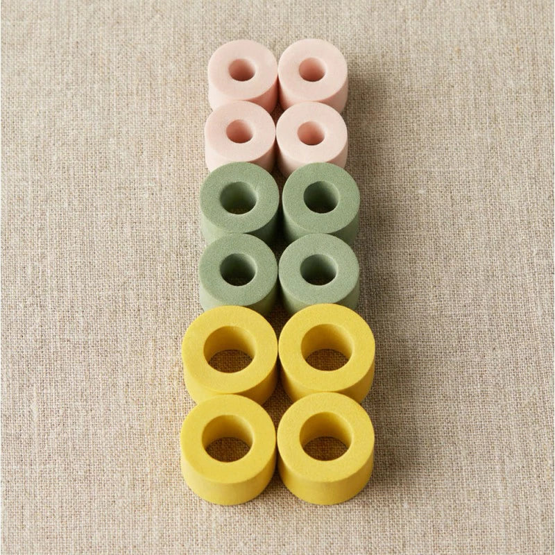 12 Maschenstopper in gelb, Grün und Rosa auf neutralem Hintergrund