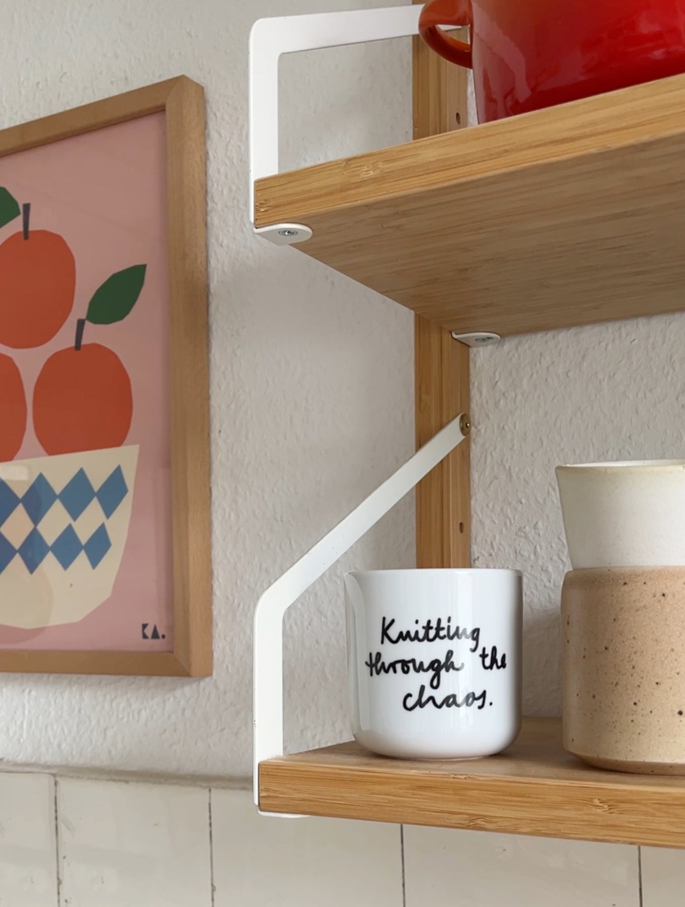 Becher ohne Griff auf Regal. Weiß mit Schriftzug Knitting through the Chaos in schwarz