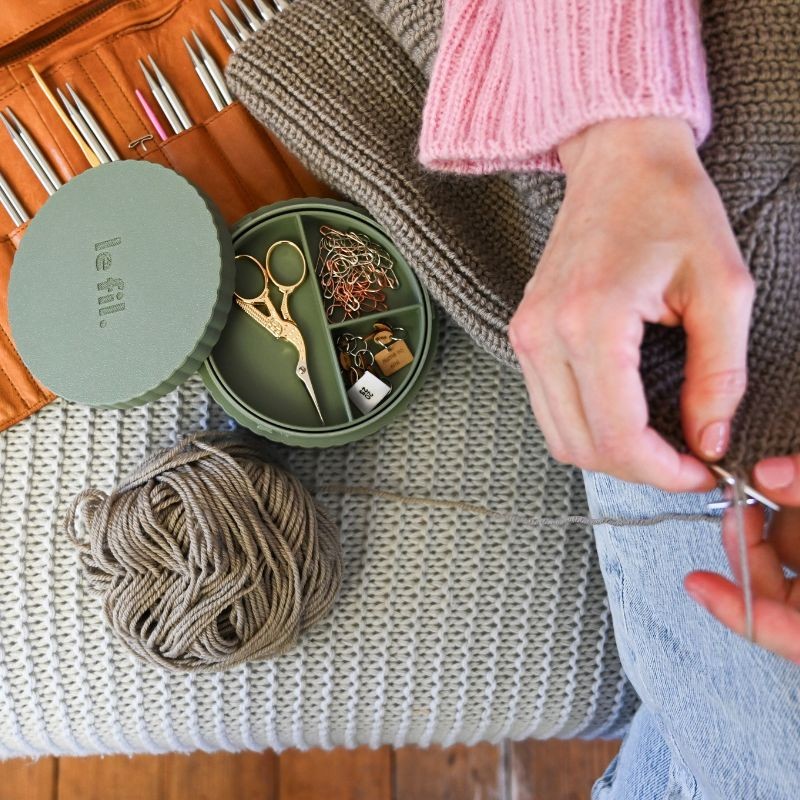 Maxi Box in grün mit Zubehör (Schere, Maschenmarkierer) gefüllt. Garn und Häde mit Stricknadeln